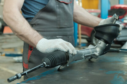 In the hands of an auto mechanic, a steering rack for a passenger car. A car service specialist monitors the technical condition of the new spare part.