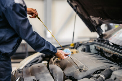 Young male car mechanic checking an engine oil on a car he is working on in his garage. Close-up.