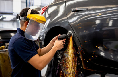 Latin American mechanic grinding a car while working at an auto repair shop and using protective workwear